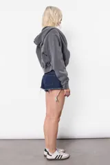 Campera gris de frisa con lavado acid, silueta oversize, manga ranglan con recortes verticales, puños de frisa con recortes de rib y mitones, cintura de rib al tono, capucha forrada al tono en su interior y bolsillo canguro. Acceso frontal mediante cierre desmontable metálico YKK con tiracierre personalizado con logo de marca.