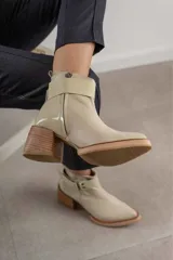 Bota corta de cuero marrón con puntera redondeada y taco cuadrado. Presenta una correa con hebilla alrededor del tobillo y cierre lateral.