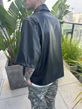Camisa negra de cuerina, corte boxy, manga corta y cuello clásico.