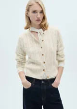 Cárdigan color crema de tejido de punto grueso con diseño trenzado y calado. Tiene cuello redondo, cierre frontal con botones y mangas largas.