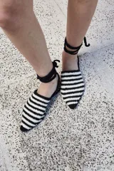 Sandalias tejidas a mano en crochet a rayas blancas y negras, con punta cerrada y tiras de cuero para atar al tobillo.