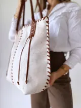 Bolso tipo tote bag de cuero color crudo con detalles de costuras y tiras de cuero marrón.