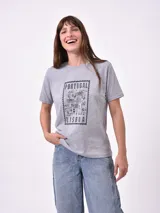 Remera blanca de algodón con cuello redondo y manga corta. Presenta un pequeño bordado en el pecho izquierdo con una figura que parece ser una persona acostada en una tabla de surf o flotador.