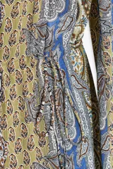 Vestido corto con estampado paisley en tonos ocre, azul y marrón. Tiene escote recto con volantes, mangas largas abullonadas con puños elásticos y cintura elástica.