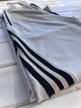 Pantalón de jogging color gris claro, corte ancho, con cordón ajustable en la cintura y tres rayas negras verticales en los laterales.