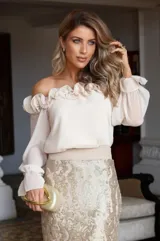Blusa beige con escote off-shoulder con volados, mangas largas abullonadas con puños elásticos y corte ajustado.