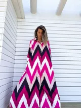 Vestido camisero largo con estampado chevron en fucsia, beige y negro, con cuello camisero, mangas largas y abotonadura frontal. Presenta aberturas laterales en el ruedo.