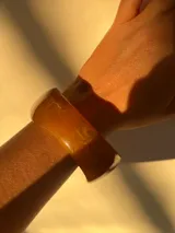 Brazalete rígido de acrílico color marrón claro con forma irregular.
