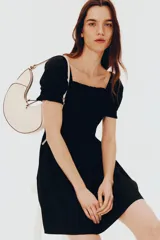 Vestido corto negro de popelina de algodón con escote cuadrado y mangas cortas abullonadas con elástico. El cuerpo es ajustado con fruncido y la falda con vuelo. Tiene ribete de volado en escote y puños.