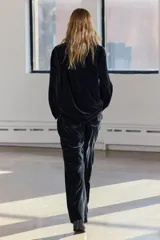 Pantalón de terciopelo negro de tiro medio, con bolsillos delanteros y traseros, pierna recta y cierre frontal con cremallera, botón y gancho metálico.