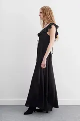 Vestido largo negro sin mangas, con escote redondo, espalda baja y volados en el escote. Ajuste en la cintura con cordón y terminaciones metálicas.