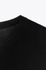 Prenda superior negra de punto liso, con cuello redondo y mangas tres cuartos. Presenta aberturas laterales en el bajo.