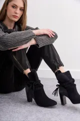 Botas de caña media de gamuza negra, con taco cuadrado y punta fina. Presenta tiras terminadas con borlas que se cruzan y atan alrededor de la caña.