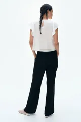 Pantalón negro de corte sastrero con cintura estándar, cierre y botón. Tiene bolsillos al bies en la parte delantera y bolsillos insertados decorativos en la parte trasera. Las piernas son acampanadas.