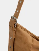 Cartera hobo color marrón claro de cuerina con correa regulable y hebilla decorativa frontal.