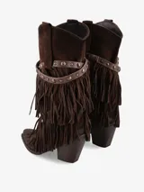 Bota de caña media de gamuza color negro, con taco medio ancho y punta ligeramente cuadrada. Presenta un detalle de flecos en capas que cubren la parte inferior de la caña y una tira de cuero con tachas metálicas plateadas rodeando el tobillo.