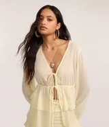 Blusa femenina de chiffon color amarillo pálido, con escote en V profundo, lazada ajustable en el centro del busto y mangas largas ajustadas. Presenta un diseño con volados en el ruedo.