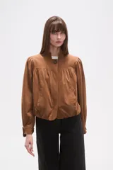 Campera marrón de manga larga con cuello mao y cierre frontal de un solo botón. Presenta pinzas y frunces en el canesú delantero y en los hombros, creando un efecto abullonado en las mangas. El bajo es ajustado con elástico.