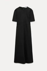 Vestido midi negro de cuello redondo y manga corta, con bolsillos laterales ocultos y costuras marcadas. Tiene corte evasé con abertura en la espalda y cierre trasero con cremallera oculta.