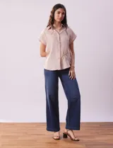 Camisa color beige con estampado de hojas marrones, de manga corta, con cuello a la base con solapa y escote en V.