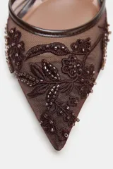 Zapato de tacón alto, destalonado, con punta fina. El cuerpo del zapato es de malla (mesh) color marrón oscuro, con apliques bordados y brillos en tonos similares. Posee una tira trasera elástica para ajuste.
