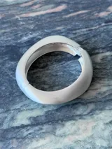 Pulsera rígida dorada con forma ovalada irregular y cierre a presión.