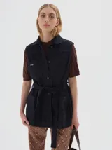 Chaleco de jean azul oscuro, con cuello camisero, cierre frontal de botones plateados, y bolsillos tipo parche en el pecho y la cadera. Incluye un cinturón de jean para ajustar la cintura.