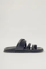 Sandalia plana negra de cuero con diseño de tiras anchas entrecruzadas sobre el empeine y una tira que separa el dedo gordo. Suela plana y gruesa.
