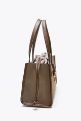 Bolso tipo shopper color marrón con doble asa corta y correa larga extraíble. Tiene detalle de pespuntes y anilla metálica decorativa. Incluye bolsa de tela interior extraíble con cierre fruncido.