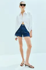 Short de denim azul de tiro alto con bolsillos delanteros y traseros. Cierre con botón y cremallera.