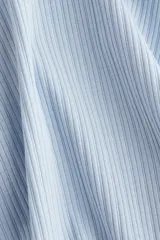 Remera ajustada de punto acanalado suave, color celeste, con manga larga, cuello redondo ribeteado en picot y tapeta de botones.