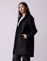 Gabardina negra impermeable con capucha desmontable, cierre central con cremallera y botones a presión, bolsillos delanteros y forro interno.
