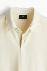 Remera polo de punto de algodón liviano color crema, de manga corta, corte ajustado y tapeta con botones.