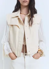 Chaleco color crema de denim con cuello camisero, cierre frontal con botones ocultos, sin mangas y corte recto.