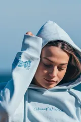 Hoodie celeste con capucha y cordones ajustables, con bordado de la frase "Glassy Waves" en el pecho y un diseño de olas en la manga.