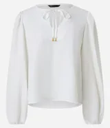 Blusa blanca de poliéster satinado, con mangas largas abullonadas, cuello con abertura en forma de gota y lazo con colgantes de corazón.