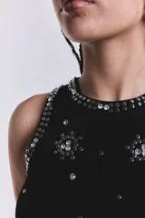 Musculosa negra de punto acanalado con cuello redondo y apliques de strass plateados en forma de flores y tachas alrededor del cuello y las sisas.