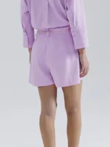 Short de lino blanco, de corte recto y tiro alto, con trabillas para cinturón y un lazo trenzado de color crudo anudado en el frente.