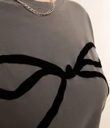 Remera gris de algodón con cuello redondo y manga corta. Presenta un estampado central de un lazo negro.