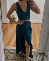 Conjunto de top y falda color verde esmeralda. El top es corto, sin mangas y con escote en V. La falda es larga con volados y abertura lateral.