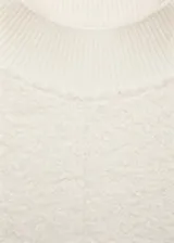 Buzo color crudo de tejido bouclé, con cuello perkins y mangas largas. Sin cierre y con terminaciones de canalé.