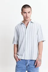 Camisa de manga corta con corte oversize, a rayas verticales blancas y grises, con cuello clásico y cierre frontal con botones. Confeccionada en algodón.