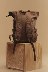 Mochila marrón de lona con detalles en cuero, cierre superior enrollable con hebillas y dos bolsillos frontales con hebilla.