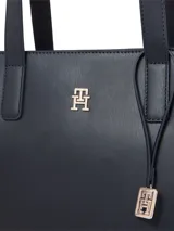Cartera tipo tote estructurada de color azul marino, confeccionada en poliuretano con forro de poliéster. Presenta asas de hombro dobles, un bolsillo interior con cremallera, un monograma TH metálico en el frente y un charm colgante desmontable con el logo TH.
