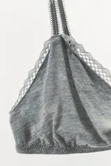 Bralette triangular gris de algodón con ribete de encaje blanco y detalle de moño rosa en el centro. Tiene tirantes finos ajustables y cierre trasero con ganchos metálicos.