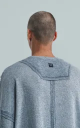 Sweater de manga larga color gris jaspeado, con cuello redondo. Presenta costuras externas decorativas y marcadas en los laterales del cuerpo y en la unión de las mangas, dándole un aspecto técnico o deconstruido.