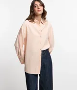 Camisa color rosa pálido, de corte amplio y alargado, confeccionada en viscosa. Tiene cuello camisero, abotonadura frontal y mangas largas con puños abotonados.