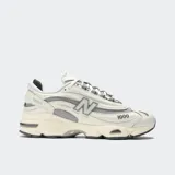 Championes New Balance modelo M1000, color crema con detalles en gris, confeccionados en cuero y malla, con logo "N" característico en los laterales y suela segmentada con amortiguación ABZORB.