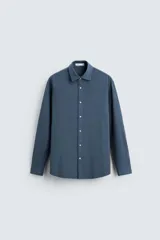 Camisa azul de corte recto, confeccionada en tejido de mezcla de algodón. Tiene cuello solapa, manga larga con puños abotonados y cierre frontal con botones.