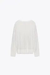 Sweater de punto calado color blanco, de corte holgado, cuello redondo y manga larga.